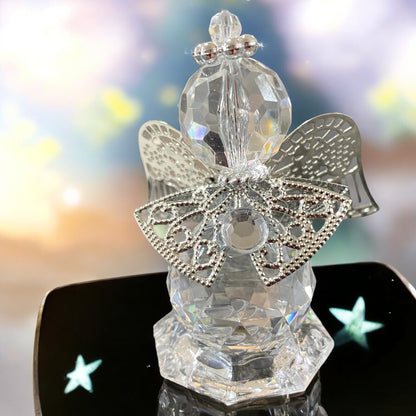 Eine kleine gläserne Deko-Engelfigur mit facettiertem Körper und silberfarbenen Flügeln sowie filigranen Verzierungen in unterschiedlichen Größen im Ambiente