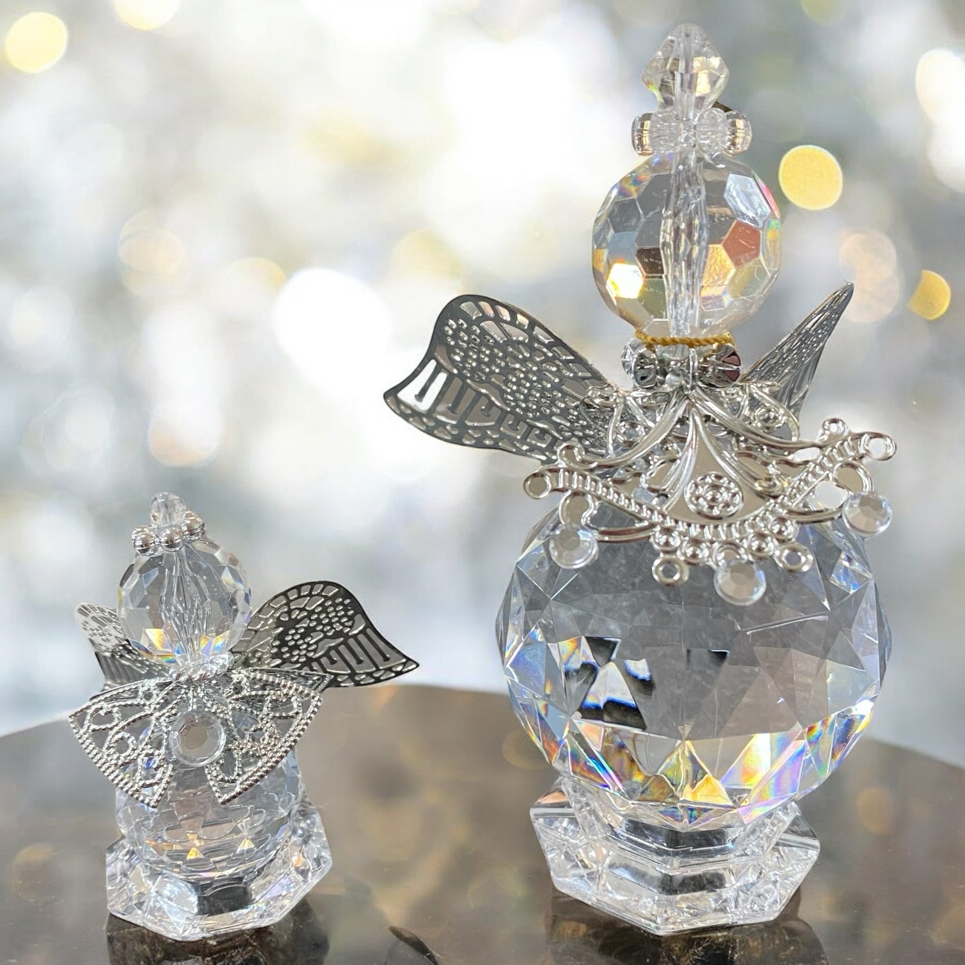 Zwei gläserne Deko-Engelfiguren mit facettiertem Körper und silberfarbenen Flügeln sowie filigranen Verzierungen in unterschiedlichen Größen im Ambiente