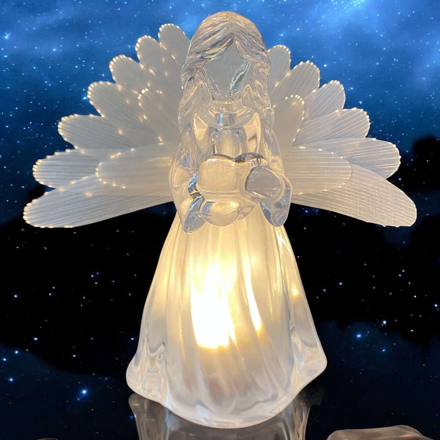 Eine transparente Acryl-Engelfigur mit Flügeln und warmweißer Beleuchtung, mit  Herz in den Händen im Ambiente
