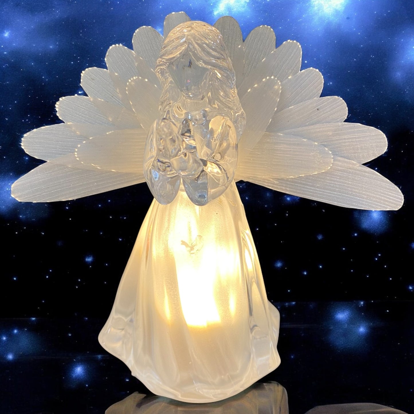 Eine transparente Acryl-Engelfigur mit Flügeln und warmweißer Beleuchtung, mit  Vogel in den Händen im Ambiente