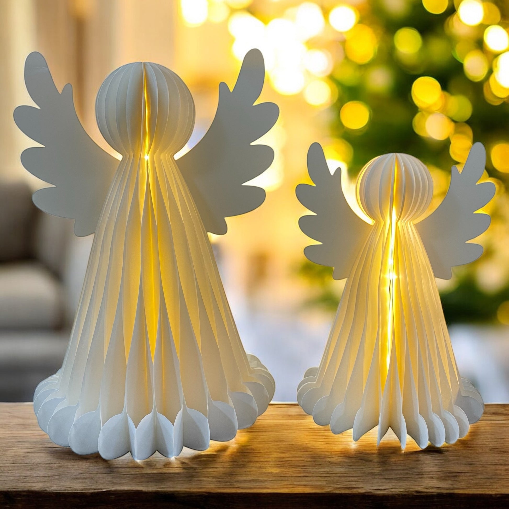 Zwei weiße Papier-Engelfiguren mit Flügeln und LED-Beleuchtung in unterschiedlichen Größen, die warm von innen leuchten im Ambiente.