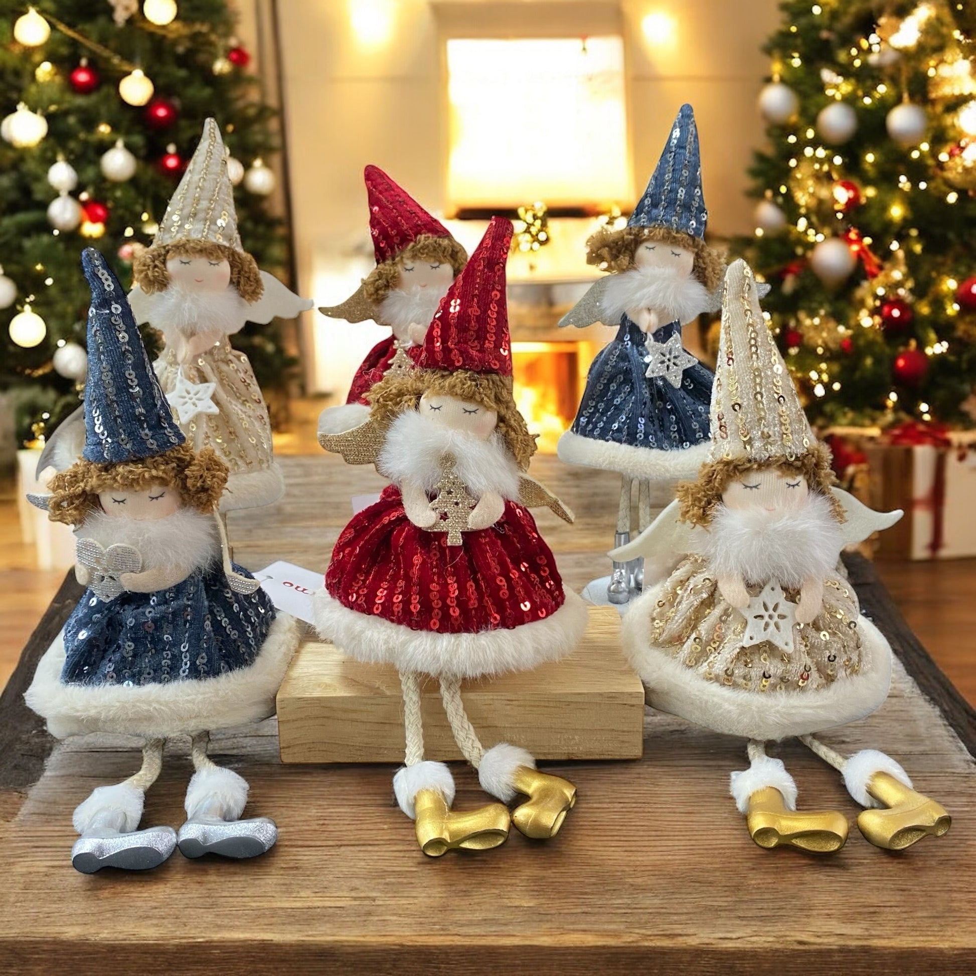 Sechs Stoff-Engelfiguren mit glitzernden Kleidern und spitzen Mützen in den Farben Gold, Rot und Blau, teils sitzend, teils stehend, mit kleinen Flügeln und goldenen oder silbernen Schuhen im Ambiente