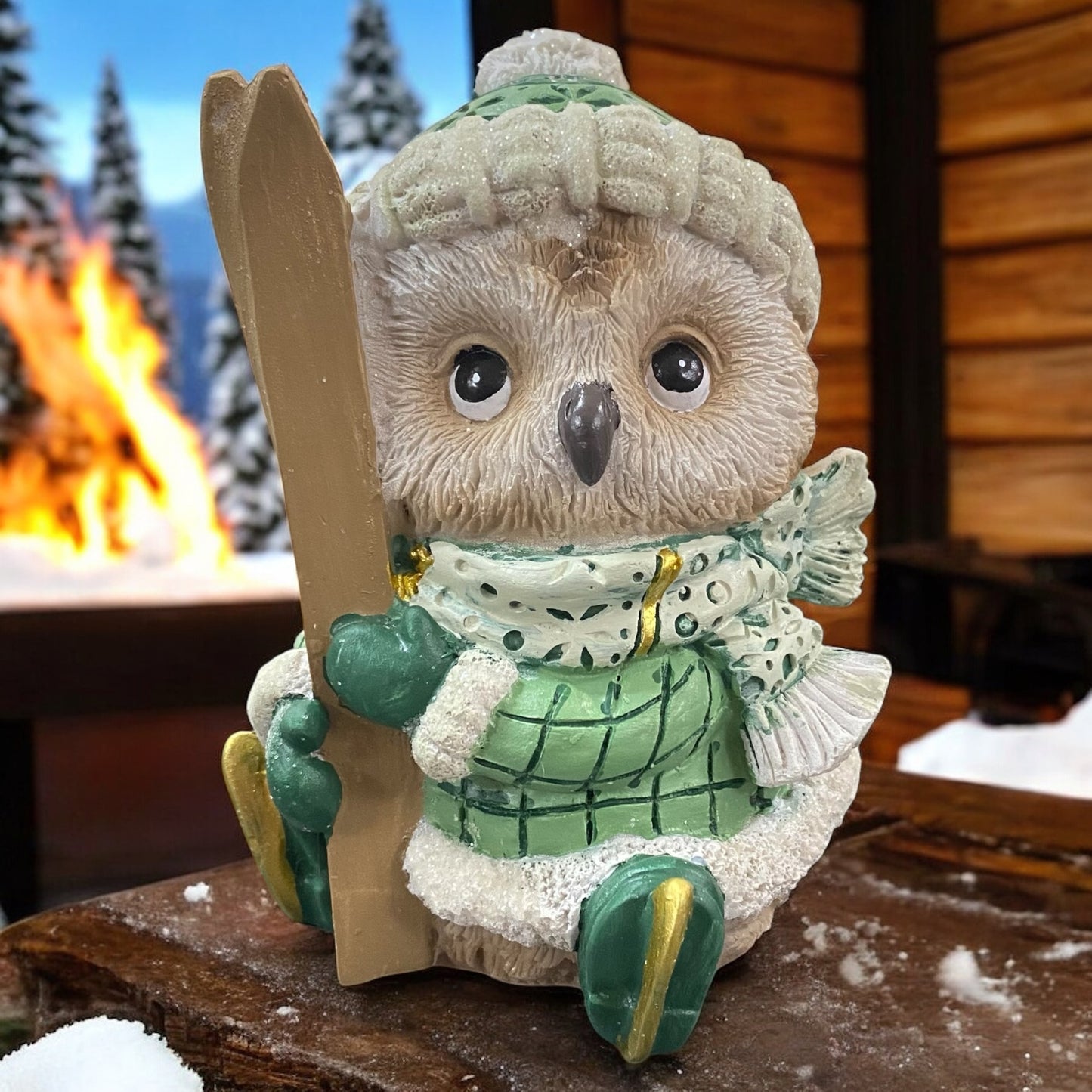 Deko-Eule in Winterkleidung mit Skiern in der Hand, liebevoll vor einer verschneiten Berghütte inszeniert.
