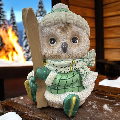 Deko-Eule in Winterkleidung mit Skiern in der Hand, liebevoll vor einer verschneiten Berghütte inszeniert.