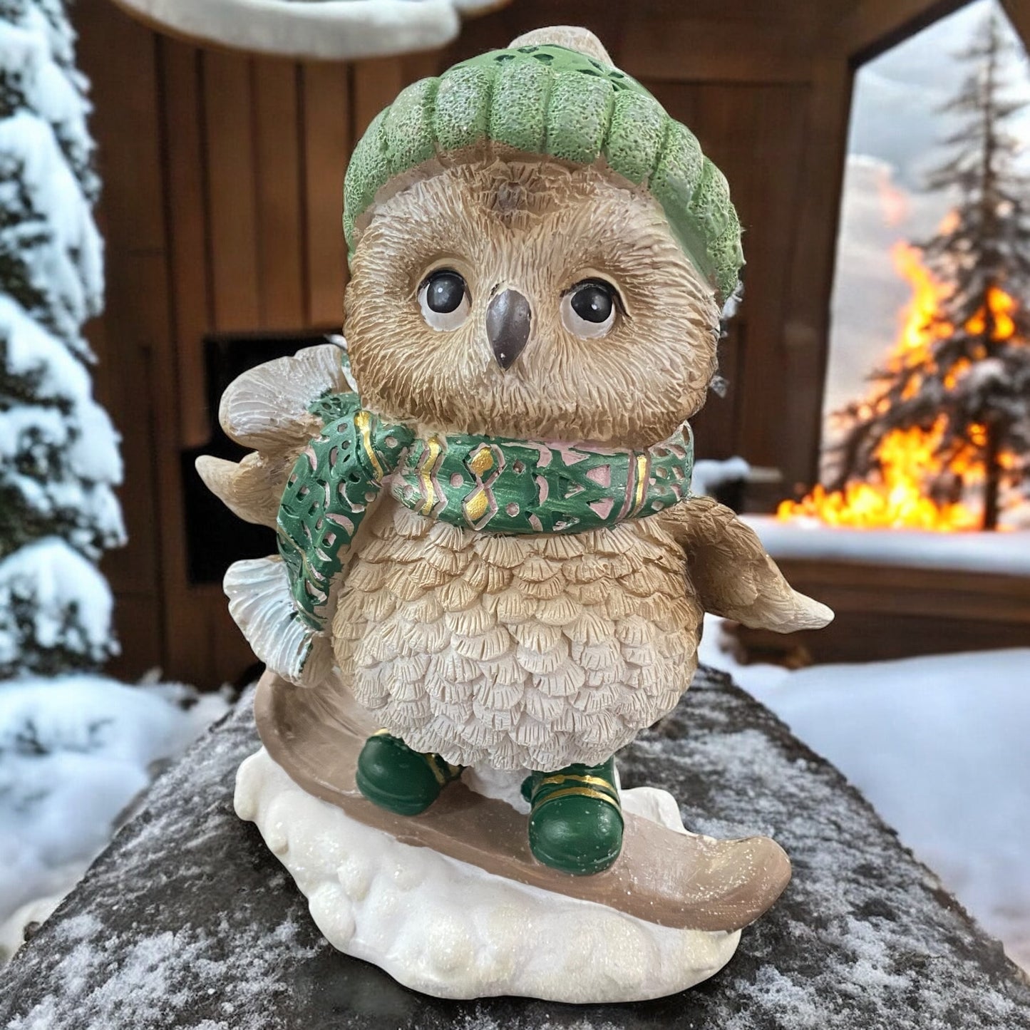 Verspielte Eulenfigur mit Snowboard, Mütze und Schal, stimmungsvoll vor verschneiter Hütte platziert.