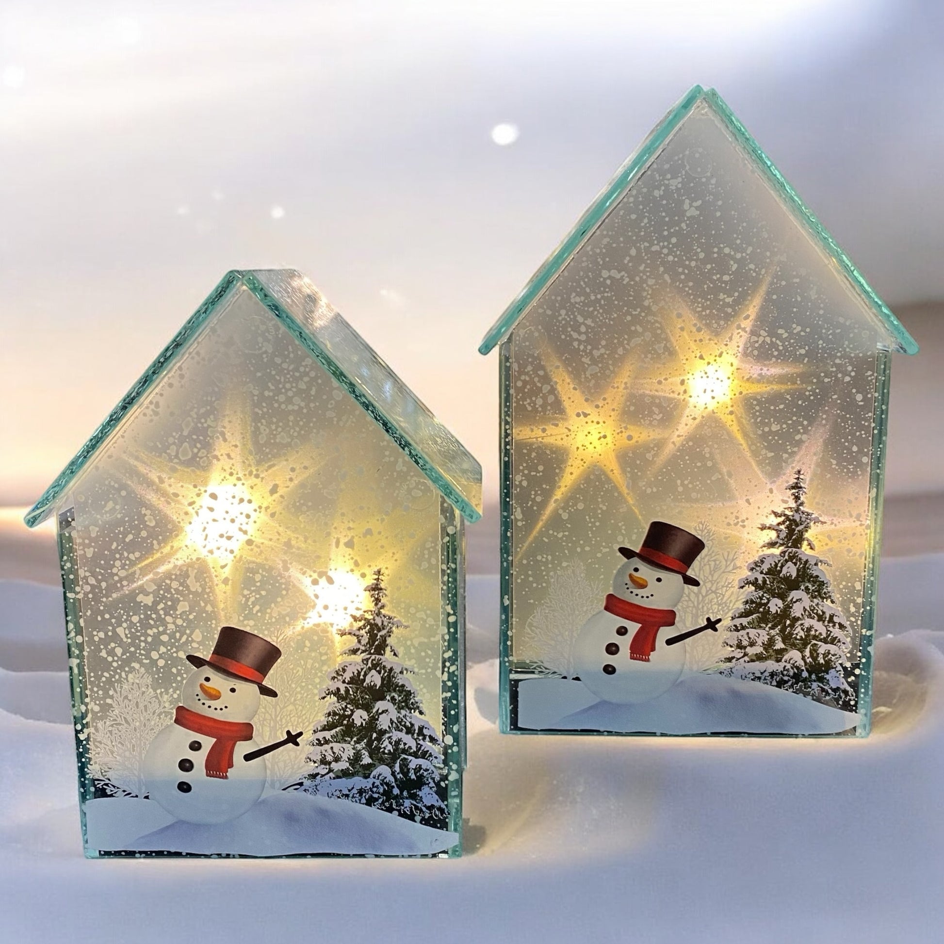 Zwei weihnachtliche Glaslichthäuser mit Schneemann- und Tannenbaum-Motiv, beleuchtet mit warmem LED-Licht im Ambiente