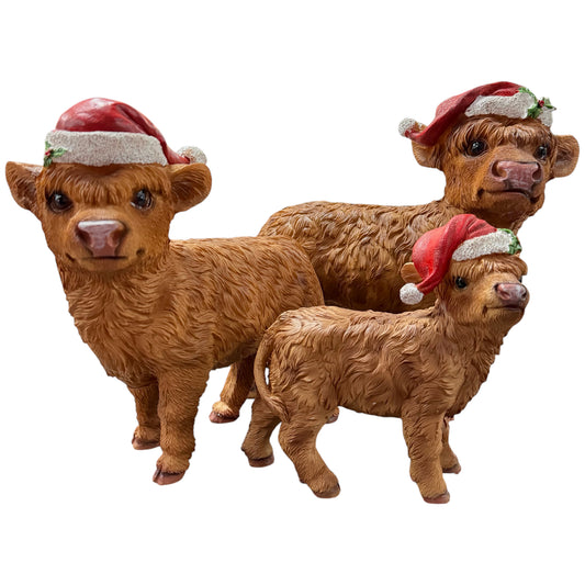 Drei Tierfiguren in Form von Hochlandrindern mit strukturierter Felloberfläche. Die Figuren tragen rote Weihnachtsmützen mit weißem Rand und stehen vor hellem, freigestelltem Hintergrund. Unterschiedliche Größen, nebeneinander angeordnet.