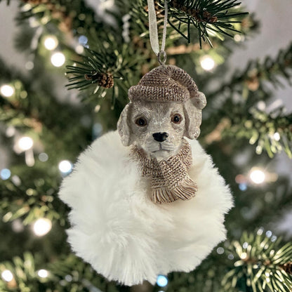 Ein dekorativer Hunde-Anhänger mit Strickmütze hängt an einem Weihnachtsbaum und ist von warmen Lichtern umgeben.