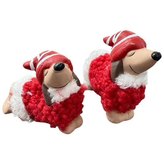 Zwei dekorative Hundefiguren in Dackelform. Die Figuren tragen rote Mützen mit weißen Streifen sowie einen roten, flauschigen Mantel mit weißen Elementen. Augen geschlossen, liegende Position. Freigestellt vor hellem Hintergrund.