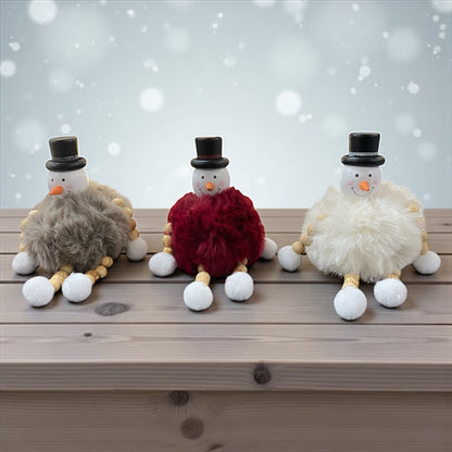 Drei sitzende Schneemannfiguren mit schwarzen Hüten und flauschigen Körpern in Grau, Rot und Weiß im Ambiente