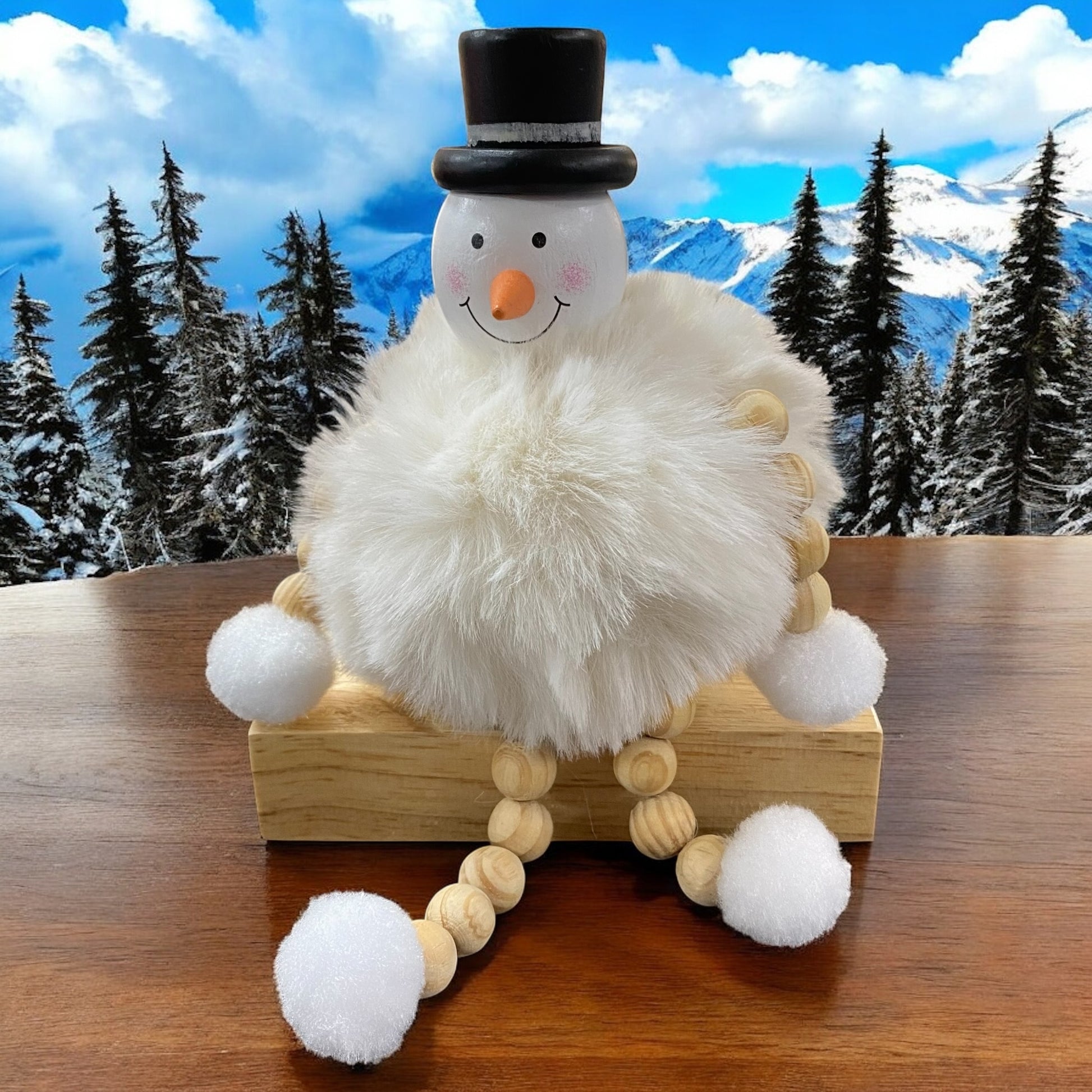 Sitzende Schneemannfigur mit schwarzem Hut und cremefarbenem, flauschigem Körper auf einem Holzblock vor verschneiter Landschaft.