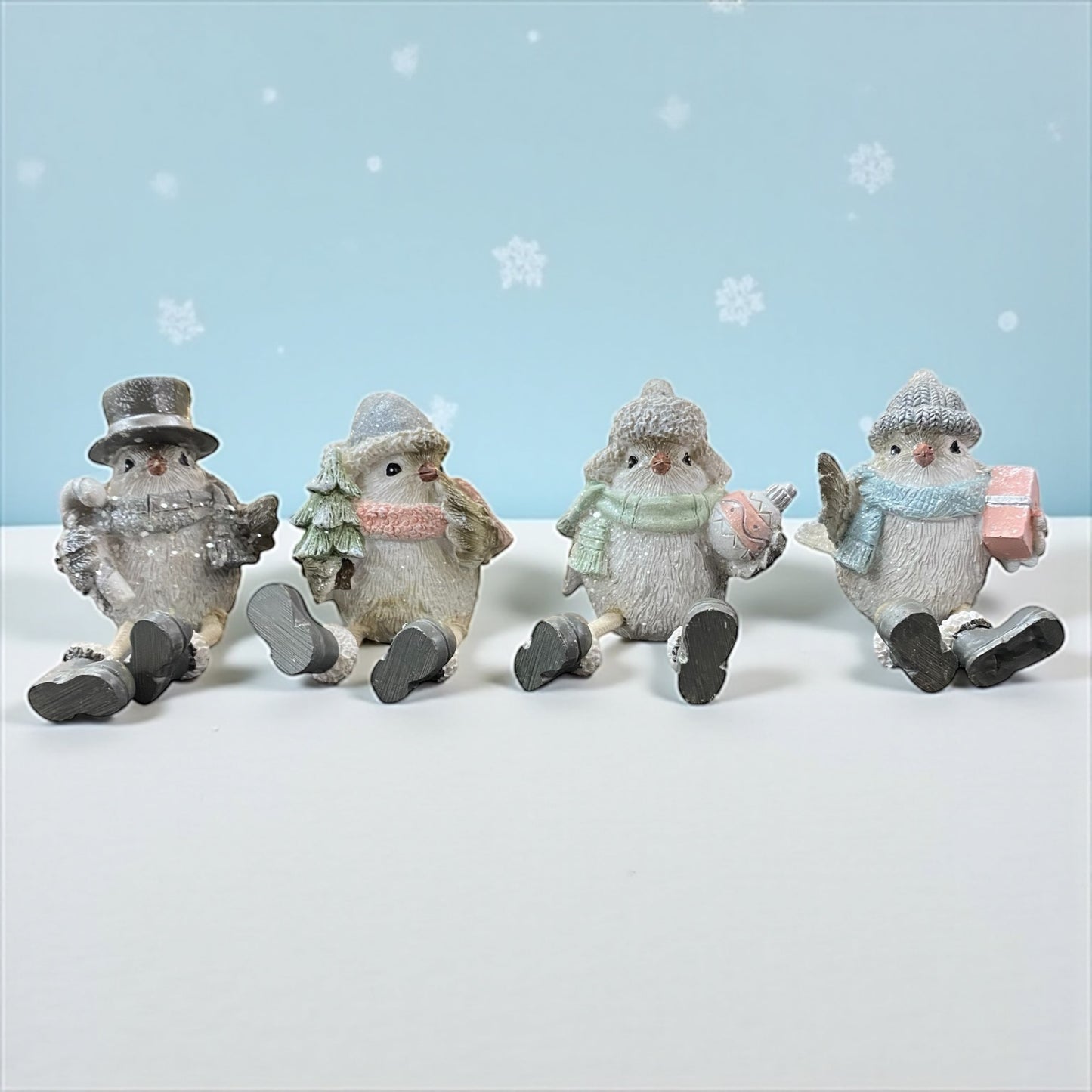 Vier sitzende Vogel-Figuren in Winterkleidung mit verschiedenen Accessoires: Zuckerstange, Tannenbaum, Christbaumkugel und Geschenk im Ambiente