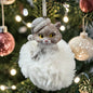 Ein Katzen-Anhänger mit Mütze auf einer weichen Plüschwolke hängt am festlich geschmückten Weihnachtsbaum.