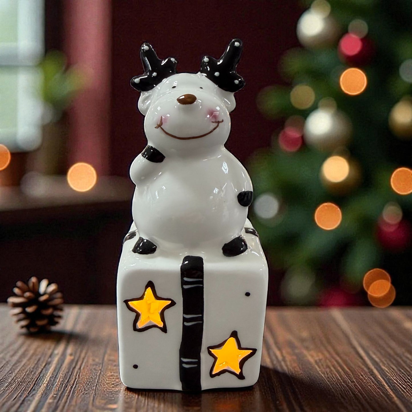 Keramik-Rentier sitzt auf einem Geschenk mit sternförmigen Aussparungen und integrierter LED-Beleuchtung.