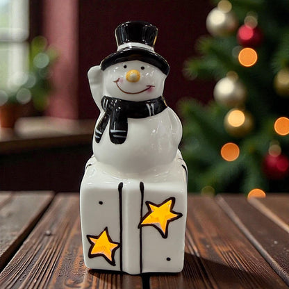 Keramik-Schneemann steht auf einem Geschenk mit sternförmigen Aussparungen und integrierter LED-Beleuchtung.