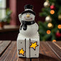 Keramik-Schneemann steht auf einem Geschenk mit sternförmigen Aussparungen und integrierter LED-Beleuchtung.