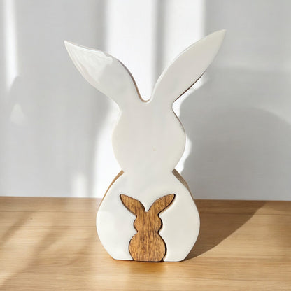 Oster-Dekoartikel in Hasenform aus Holz. Ein großer weißer Osterhase mit weißem Keramik Überzug, worin ein kleiner Holz Osterhase zu sehen ist, im Ambiente