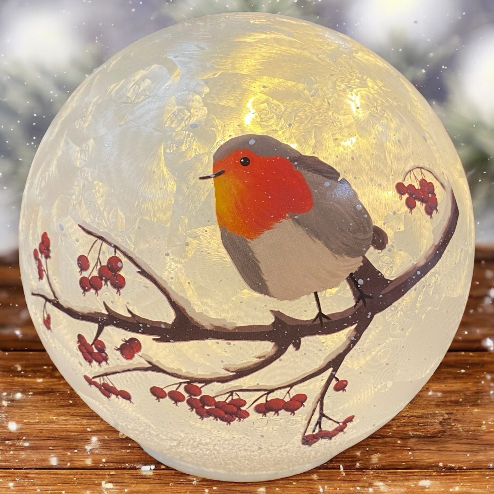 Leuchtende Formano Glaskugel mit Vogelmotiv auf Zweig, stimmungsvoll auf Holztisch im Winterambiente dekoriert.