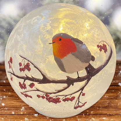 Leuchtende Formano Glaskugel mit Vogelmotiv auf Zweig, stimmungsvoll auf Holztisch im Winterambiente dekoriert.