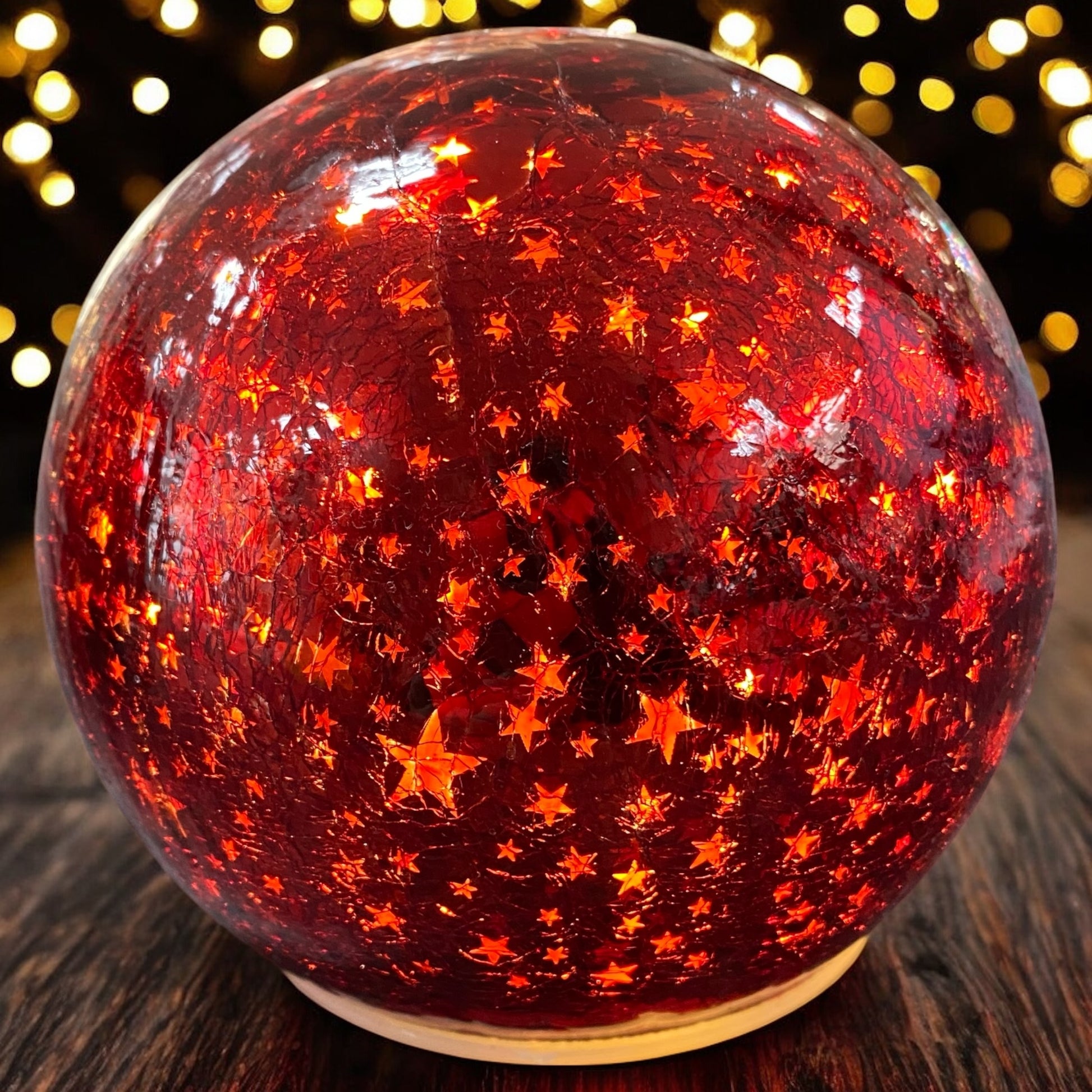 Leuchtende rote Crackle-Glas-Kugel mit goldenen Sternenmotiven, strahlend im warmen Licht eines weihnachtlichen Ambientes.