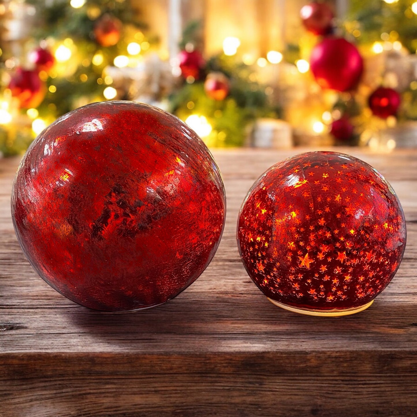 Zwei leuchtende rote Crackle-Glas-Kugeln mit goldenen Sternen auf einem Holztisch vor warmem Lichterhintergrund.
