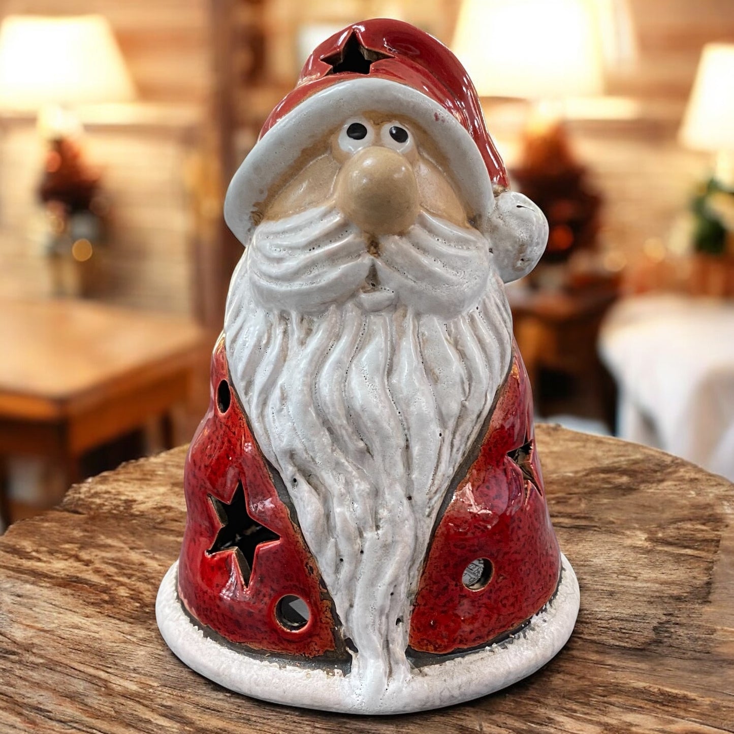 Breite Keramikfigur eines Weihnachtsmanns mit rotem Mantel und ausgestanzten Sternen als Teelichthalter, auf einem Holztisch in weihnachtlicher Umgebung.