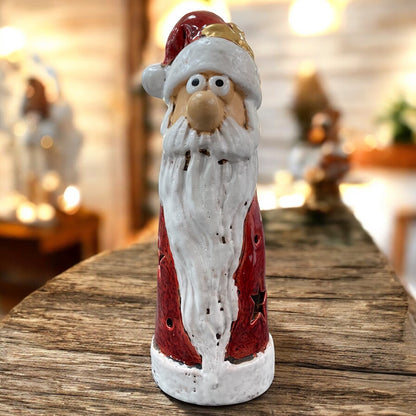 Schmale Keramikfigur eines Weihnachtsmanns mit rotem Mantel und langen weißem Bart als Teelichthalter, auf einem Holztisch mit festlicher Beleuchtung.