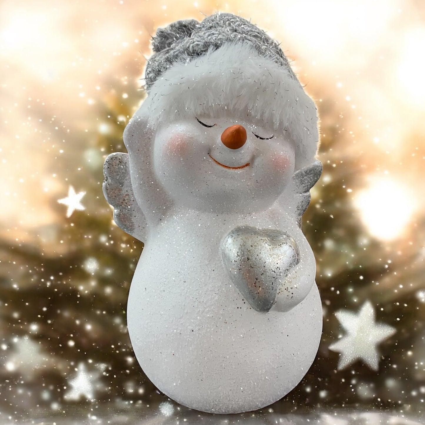 Keramik-Schneemann mit silbernem Herz in den Händen, steht vor warm leuchtendem Hintergrund mit funkelnden Sternen.