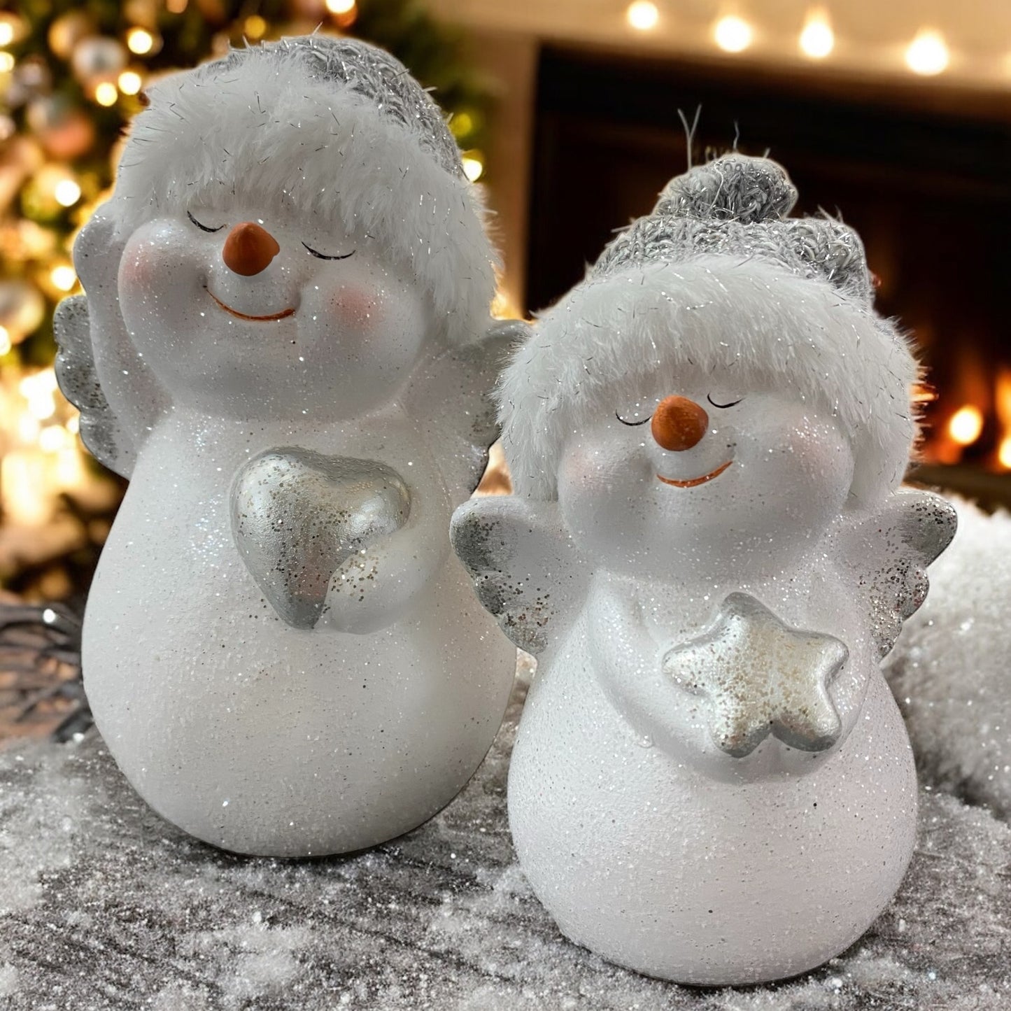 Zwei weiße Schneemannfiguren mit silbernen Flügeln und Mützen, eine hält ein Herz, die andere einen Stern im Ambiente