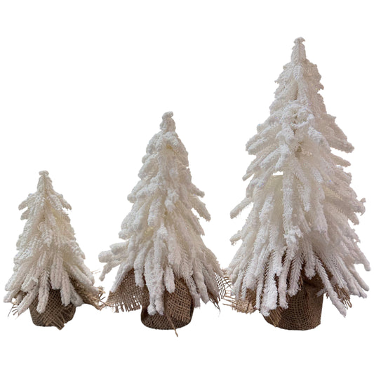 Drei weiße, schneebedeckte Dekotannenbäume in unterschiedlichen Größen stehen nebeneinander und sind jeweils in einen kleinen Jutebeutel eingesetzt.