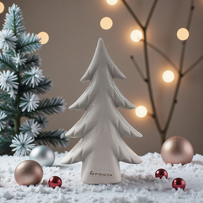 Ein einzelner cremeweißer Keramik-Tannenbaum steht auf einer dekorativen Schneefläche, umgeben von Kugeln und einer kleinen Tanne im Hintergrund.