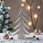 Ein einzelner cremeweißer Keramik-Tannenbaum steht auf einer dekorativen Schneefläche, umgeben von Kugeln und einer kleinen Tanne im Hintergrund.