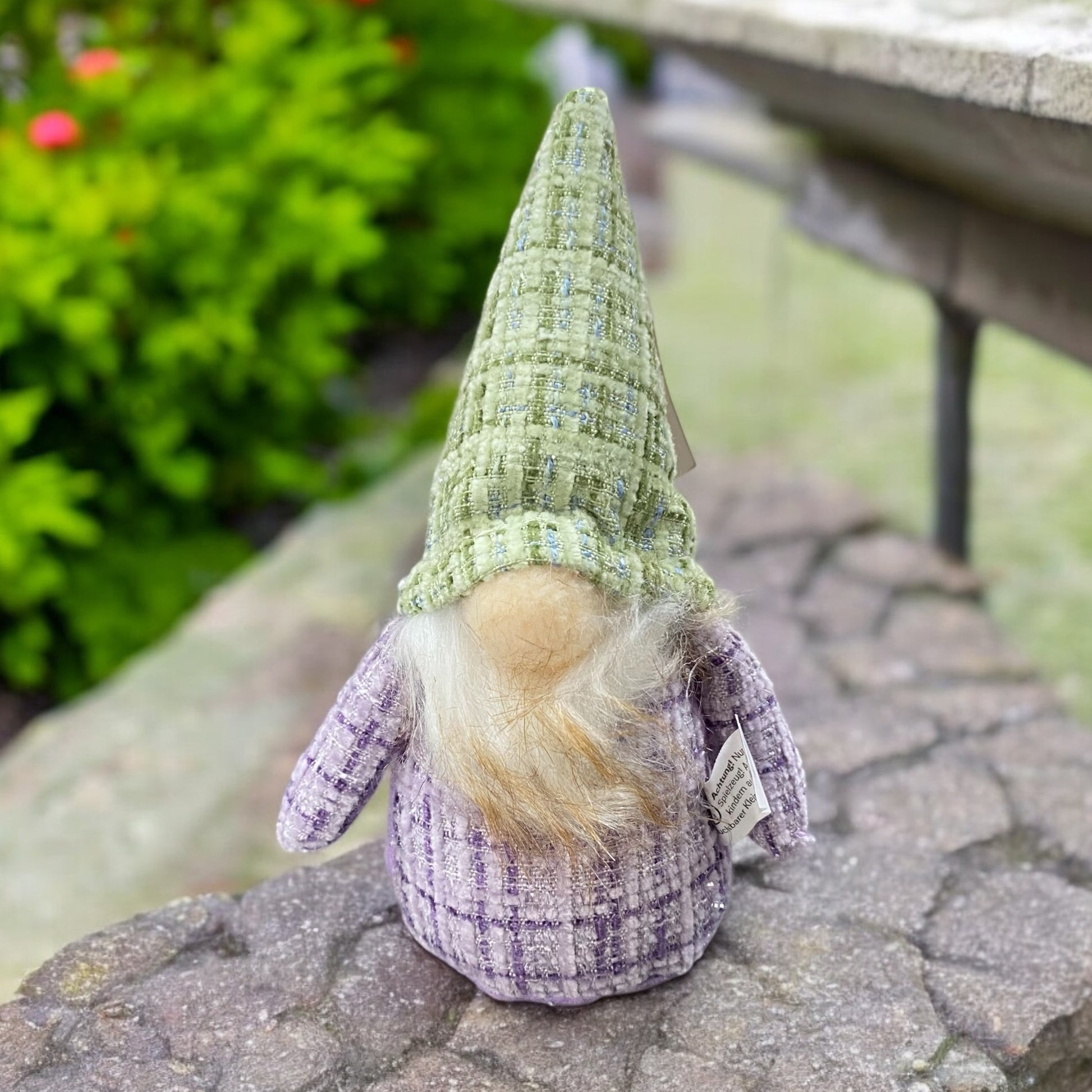 Ein kleiner Deko Stoff Wichtel zum Aufstellen mit grüner Zipfelmütze und lila Körper im Ambiente