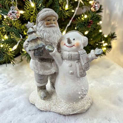 Eine dekorative Figur mit Nikolaus und Schneemann steht vor einem beleuchteten Weihnachtsbaum auf einer schneebedeckten Fläche.