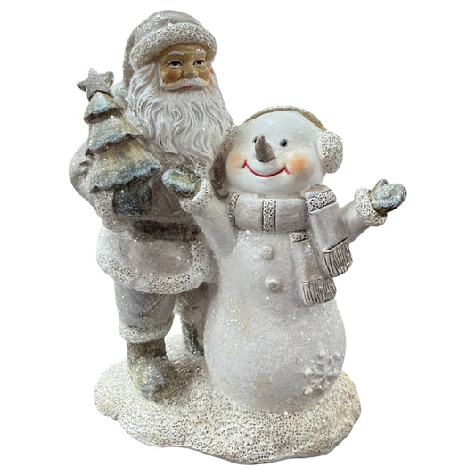 Eine winterliche Dekofigur zeigt einen Nikolaus mit Tannenbaum neben einem lächelnden Schneemann auf verschneitem Sockel.