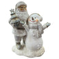 Eine winterliche Dekofigur zeigt einen Nikolaus mit Tannenbaum neben einem lächelnden Schneemann auf verschneitem Sockel.