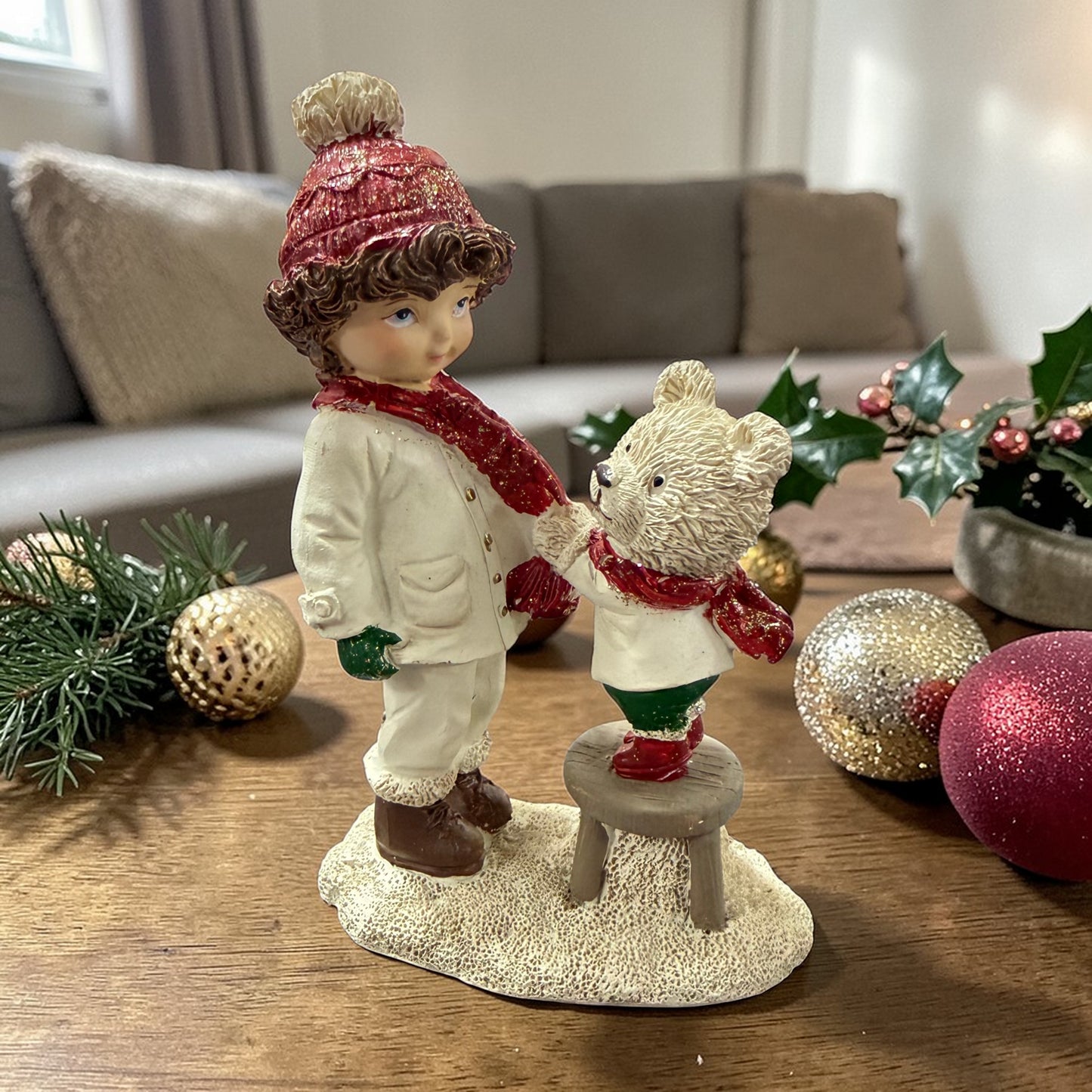 Eine dekorative Figur zeigt ein Kind, das einem Teddybären auf einem Hocker gegenübersteht.