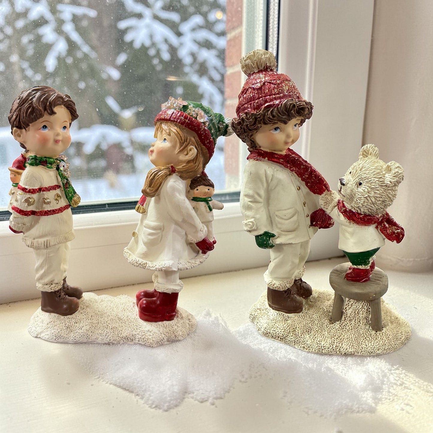 Zwei dekorative Figuren zeigen Kinder in winterlicher Kleidung sowie ein weiteres Kind mit einem Teddybären auf einem Hocker.