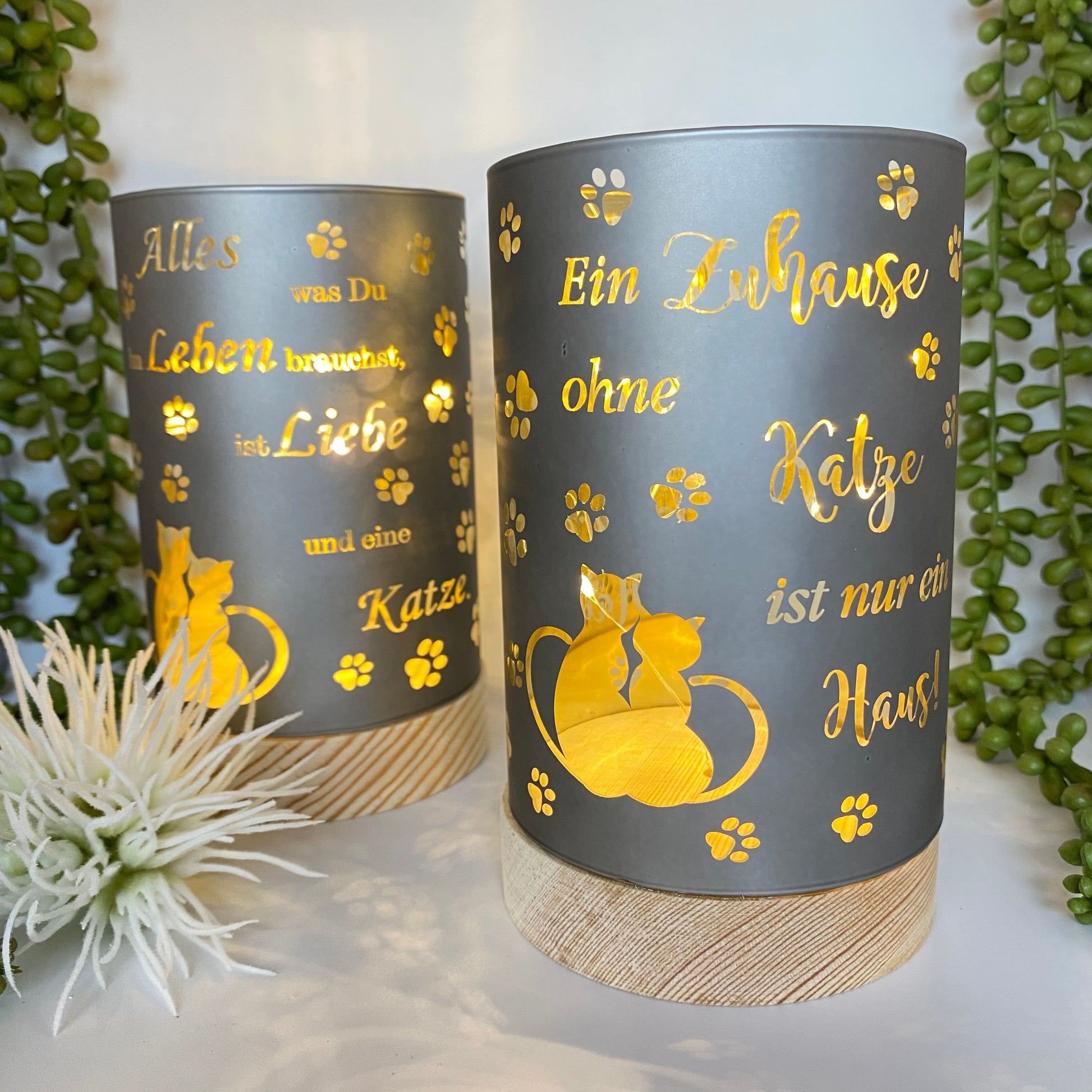 Zwei Taupe-farbende LED Säulen mit Holz Sockel. Auf dem Dekolicht ist eine Katze und jeweils ein Spruch abgebildet in goldener Schrift. Die Dekolichter sind beleuchtet im Ambiente platziert.