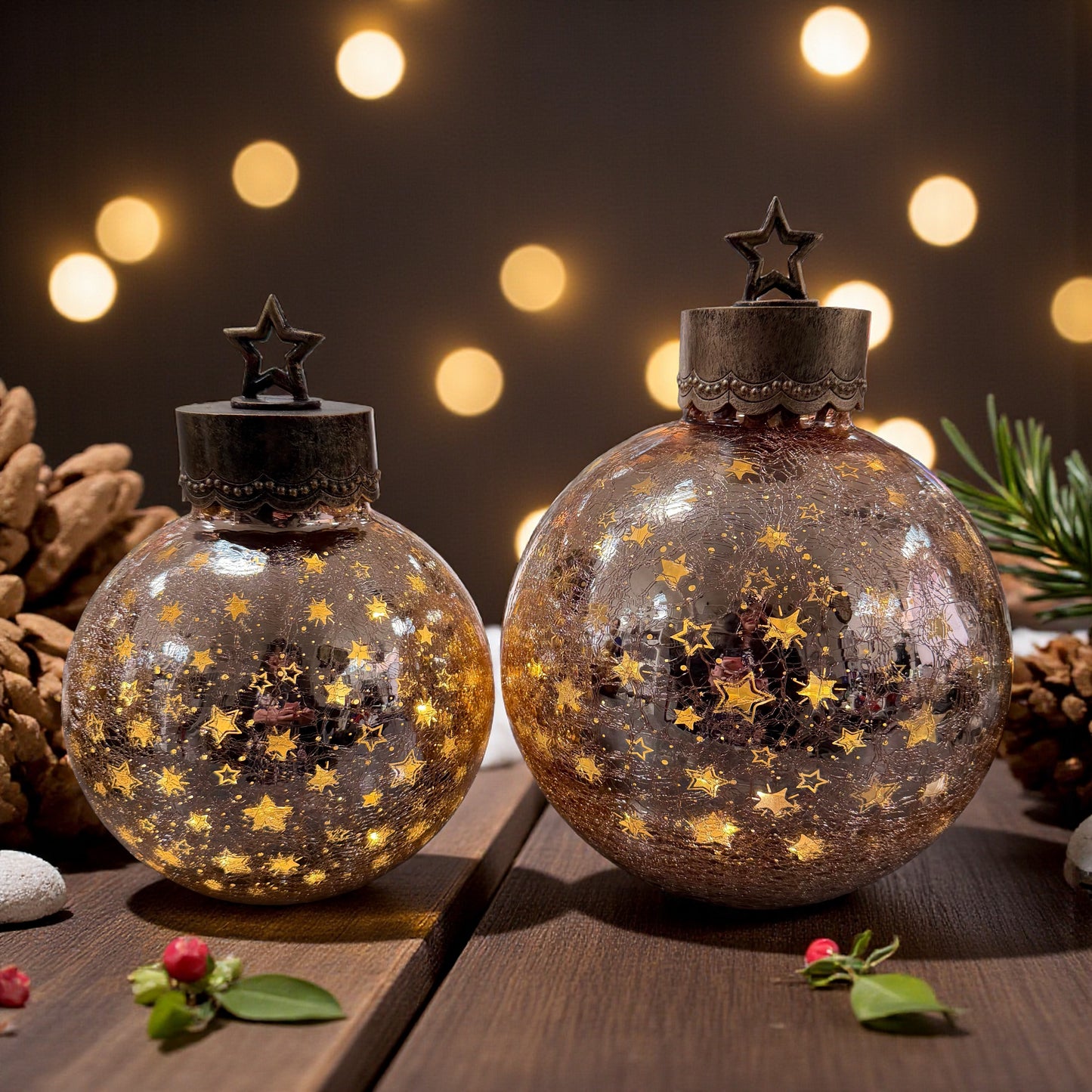 Zwei kugelförmige Dekoleuchten aus crackle Glas mit Sternmuster und Metallkappen mit Stern stehen auf einem Holztisch vor einer Lichterkette und weihnachtlicher Dekoration.