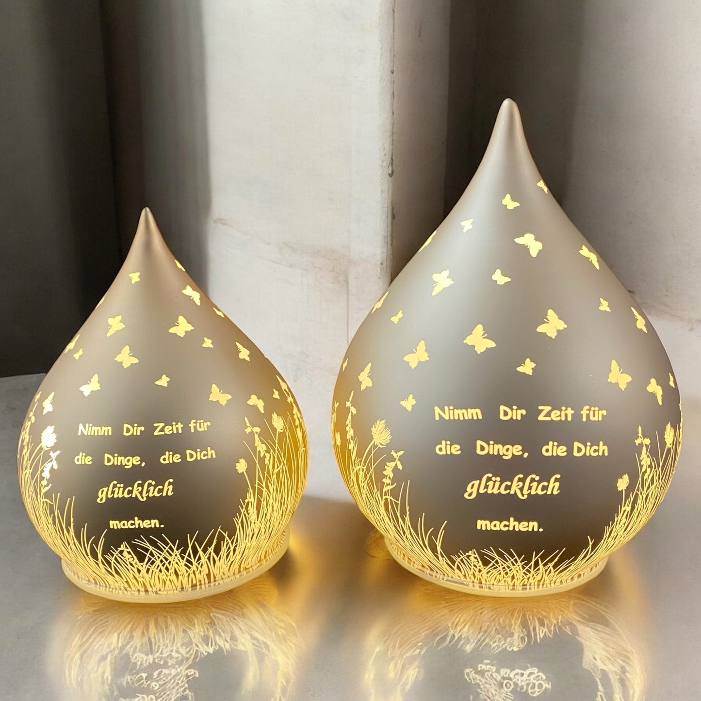 Zwei lachs-farbene Dekolicht Tropfen aus Glas mit Spruch "Nimm dir Zeit für die Dinge, die dich glücklich machen" beleuchtet im Ambiente