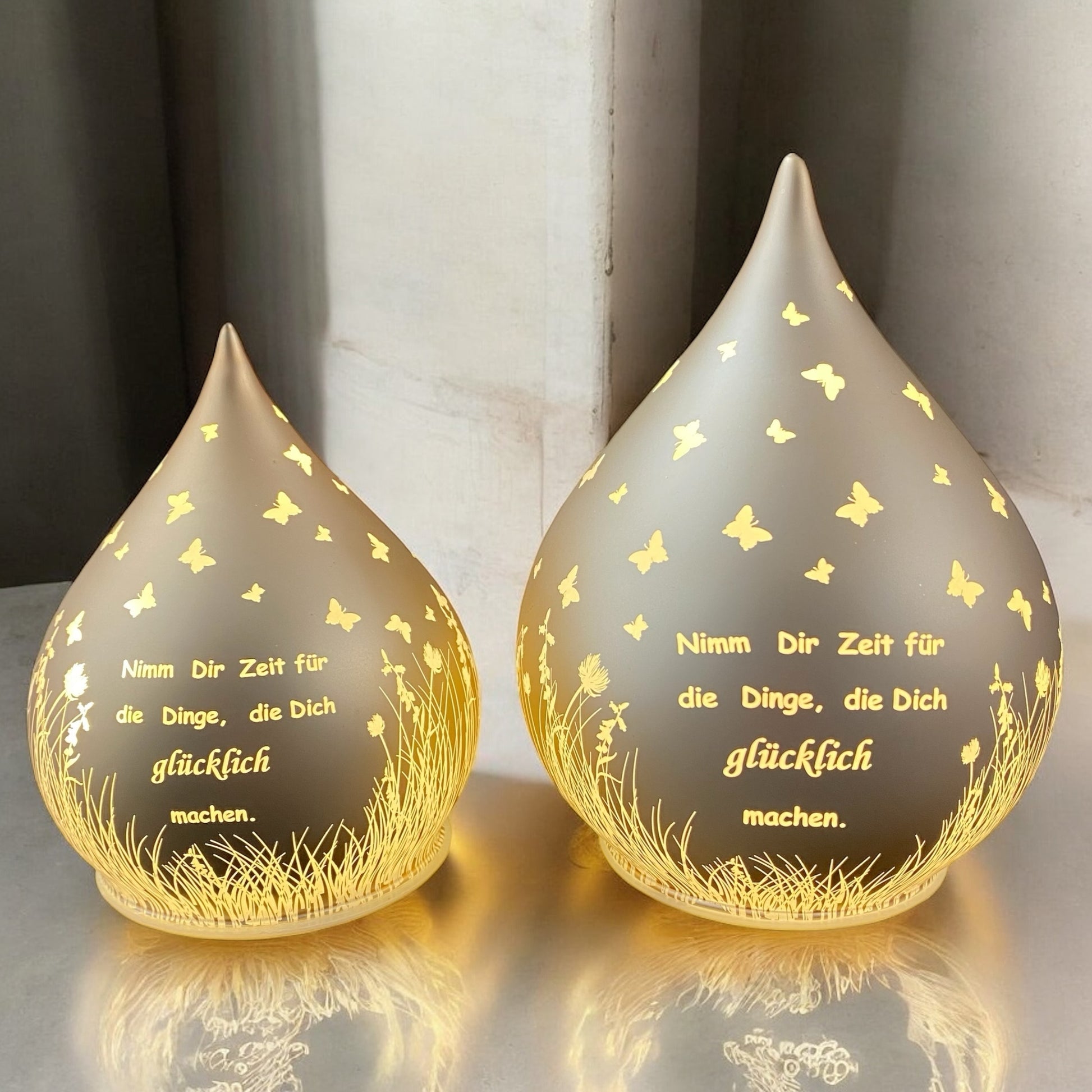 Zwei lachs-farbene Dekolicht Tropfen aus Glas mit Spruch "Nimm dir Zeit für die Dinge, die dich glücklich machen" beleuchtet im Ambiente