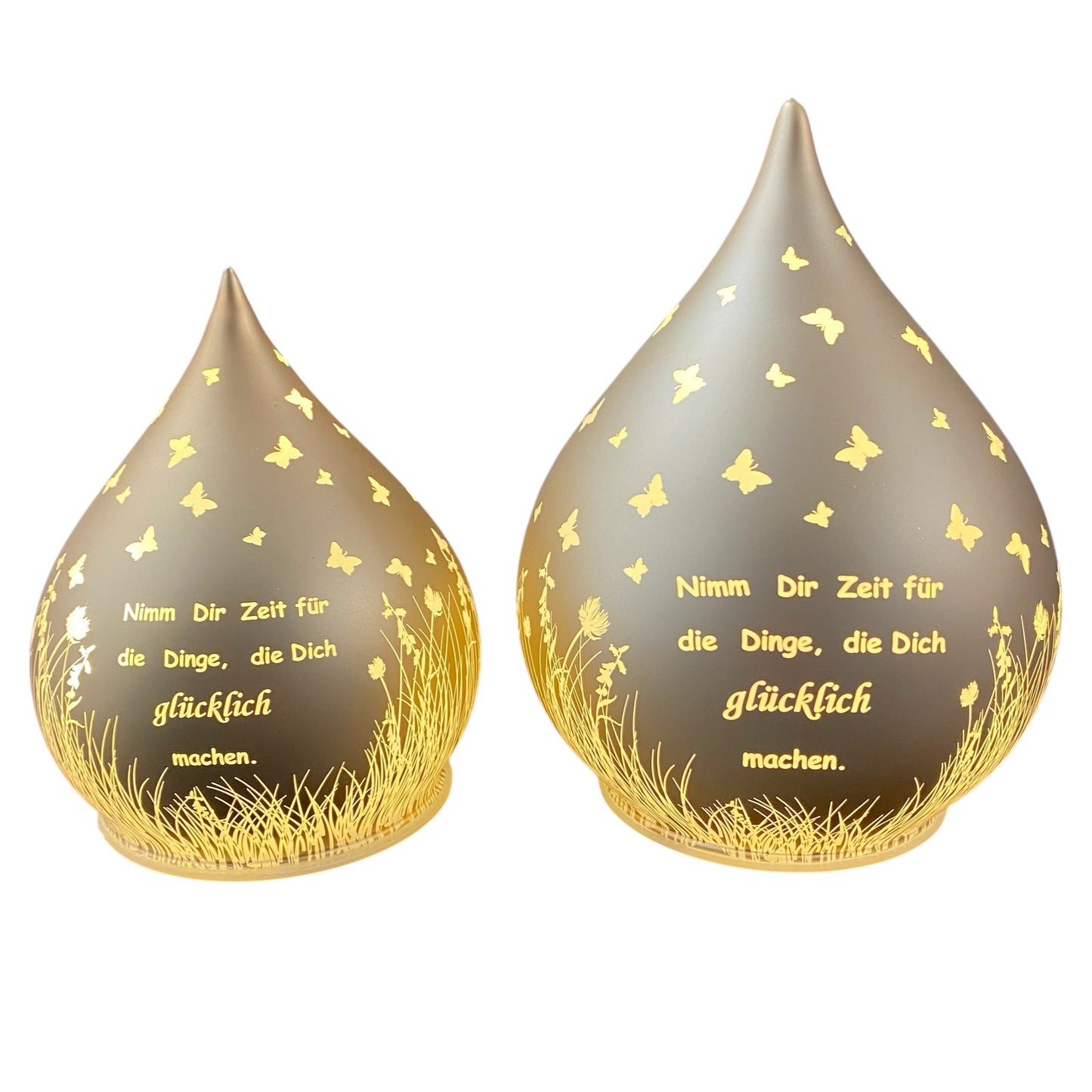 Zwei lachs-farbene Dekolicht Tropfen aus Glas mit Spruch "Nimm dir Zeit für die Dinge, die dich glücklich machen" vor weißem Hintergrund