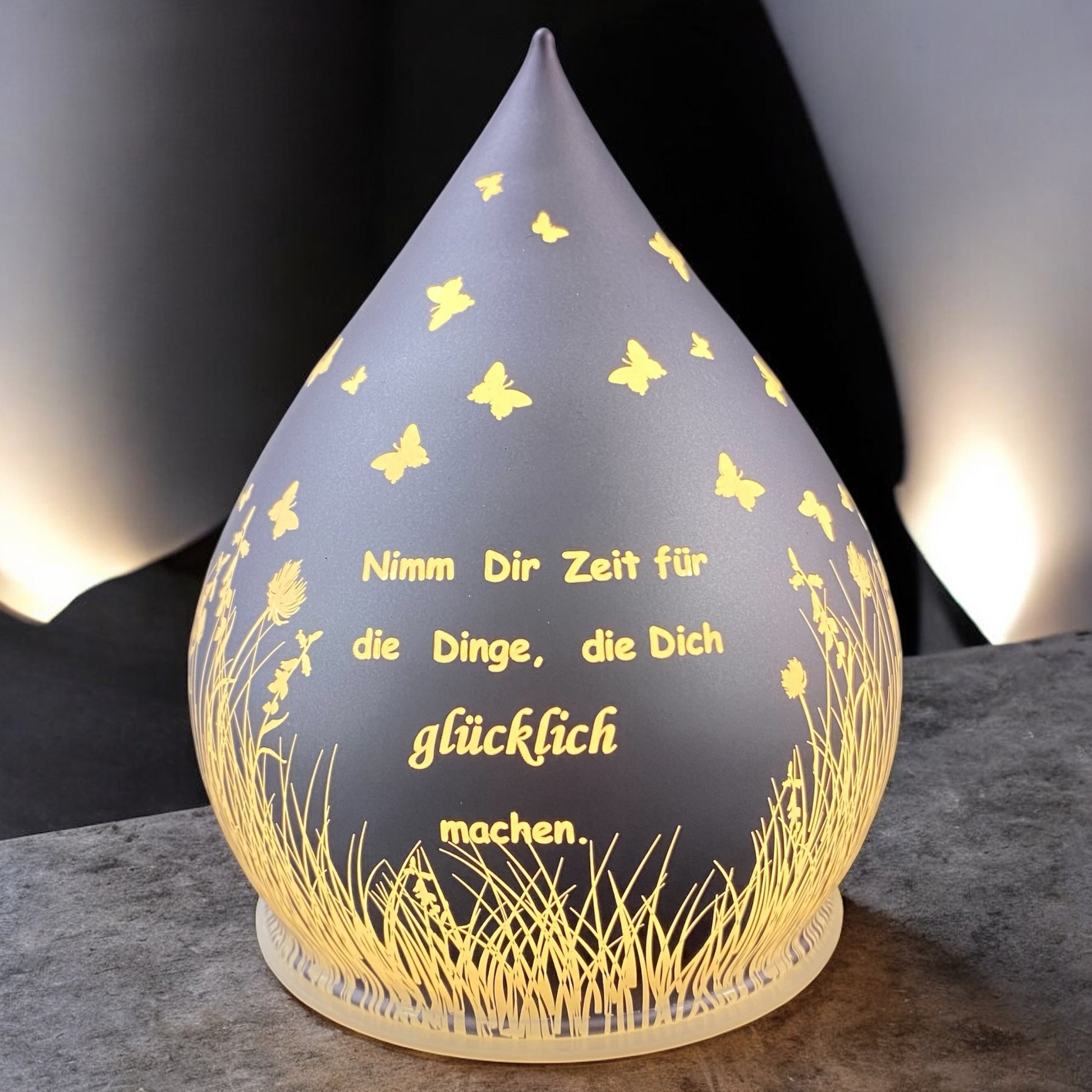 Ein lila-farbener Dekolicht Tropfen aus Glas mit Spruch "Nimm dir Zeit für die Dinge, die dich glücklich machen" im Ambiente