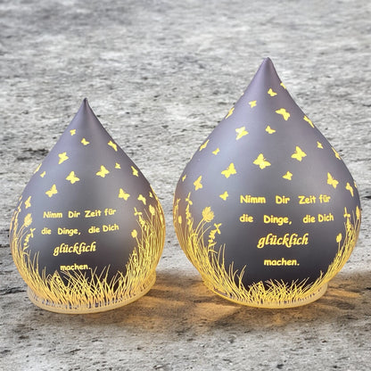 Zwei lila-farbene Dekolicht Tropfen aus Glas mit Spruch "Nimm dir Zeit für die Dinge, die dich glücklich machen" im Ambiente