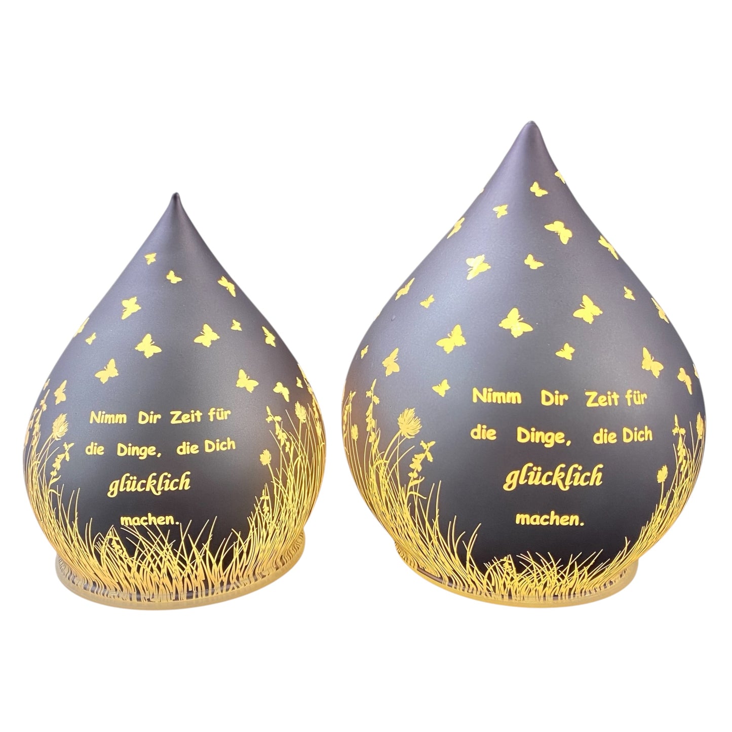 Zwei lila-farbene Dekolicht Tropfen aus Glas mit Spruch "Nimm dir Zeit für die Dinge, die dich glücklich machen" vor weißem Hintergrund