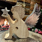 Holzfigur in Form eines Engels mit silberfarbenen Flügeln und einem Stern in der Hand vor einem Kamin und weihnachtlicher Dekoration.