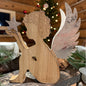 Holzfigur in Form eines Engels mit silberfarbenen Flügeln und einem Stern in der Hand auf einer dekorierten Oberfläche vor weihnachtlichem Hintergrund.