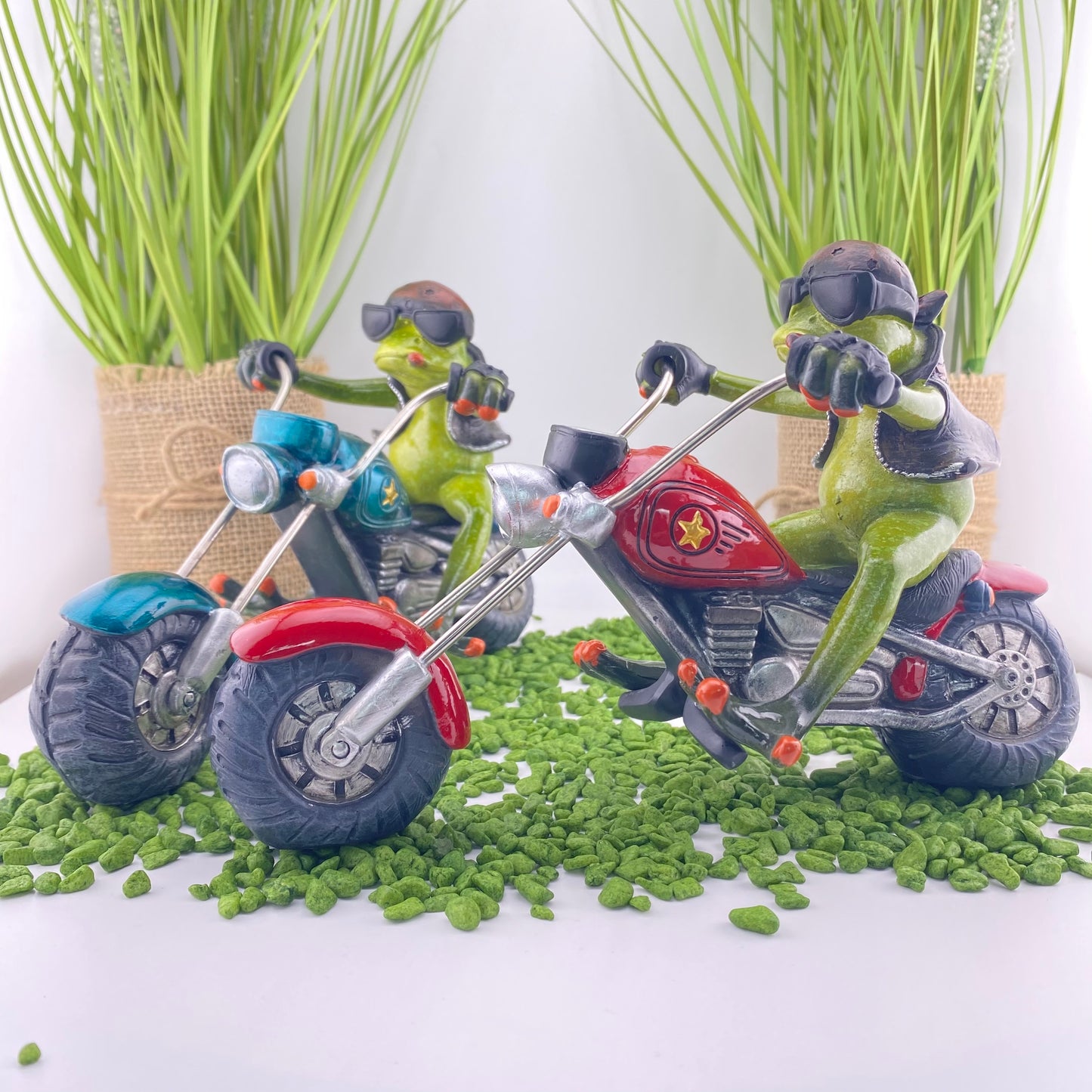 Zwei Dekofigur Frosch-Männer der Serie Froschhausen sitzen auf einem rotem und blauen Motorrad. Die Froschdekoration Biker ist im Ambiente platziert.