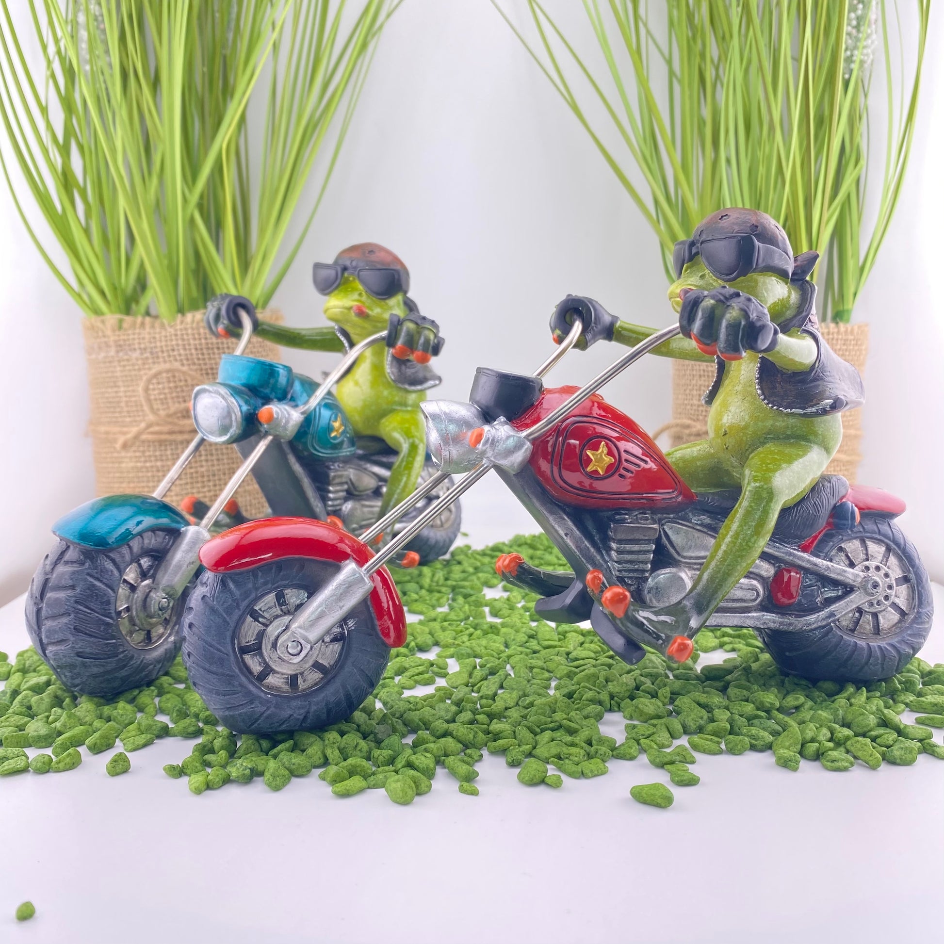 Zwei Dekofigur Frosch-Männer der Serie Froschhausen sitzen auf einem rotem und blauen Motorrad. Die Froschdekoration Biker ist im Ambiente platziert.